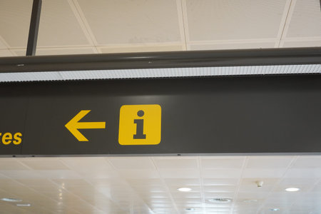 Yellow information sign with arrow pointing left hanging from ceiling in airport terminalの写真素材