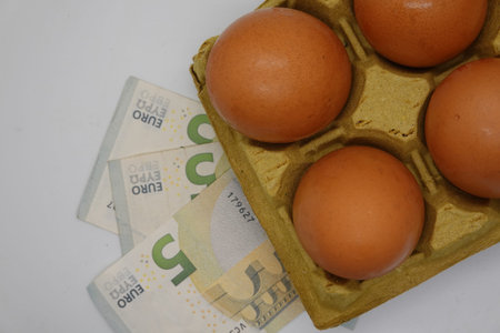 Euro banknotes lying under a carton of four eggs represent the increasing cost of food and rising inflationの写真素材