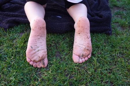 Dirty children's feet resting on green grass, evoking carefree summer days and connection with natureの写真素材