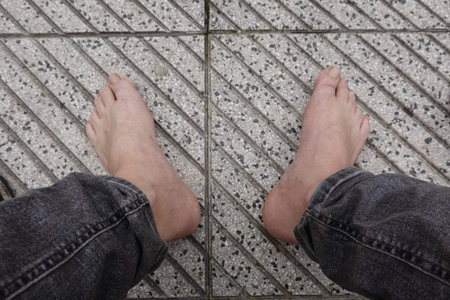 Man wearing jeans standing barefoot on textured pavement tiles, enjoying freedom and connection with...