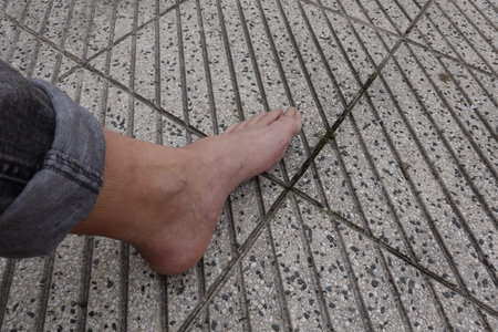 Man resting comfortably on textured, patterned paving tiles, with bare foot resting on the ground...