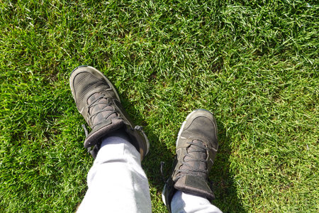 Pov shot of a man wearing trekking shoes about to step barefoot on a vibrant green grass lawn,...
