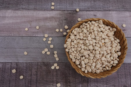 Numerous dried lupine beans are overflowing into a wicker basket placed on a rustic wooden table,...