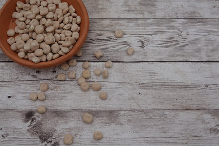 Lupine beans scattered from a terracotta bowl onto a weathered wooden surface, creating a rustic and organic ambianceの写真素材