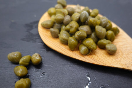 Capers, pickled in vinegar brine, sit on a wooden spoon, ready to add a burst of salty, tangy flavor to Mediterranean dishesの写真素材
