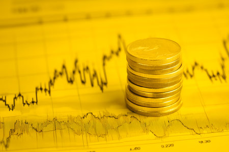 Golden coins stacked on a yellow stock market chart showing rising trend, representing successful investment and financial growthの素材