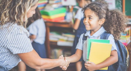 Happy elementary school student shaking hands with her teacher in a bright classroom, celebrating a warm welcome on the first day of schoolの素材
