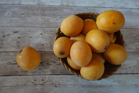 Ripe loquats, also known as Japanese medlars or Japanese plums, are overflowing a wicker basket set...