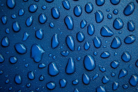 Close-up of glistering water droplets beading on a textured, waterproof blue surface, showing the hydrophobic properties of the materialの素材