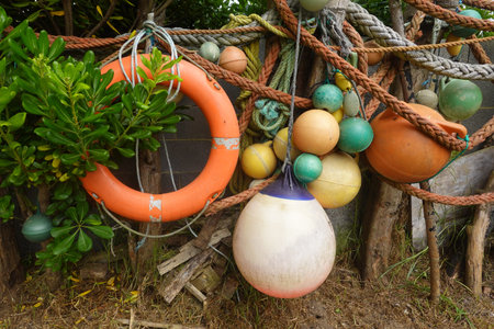 Vibrant orange lifebuoy, colorful fishing buoys, and tangled rope forming a captivating nautical...