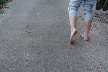 Close-up of man's feet walking barefoot on a gray asphalt road, enjoying the connection with natureの写真素材
