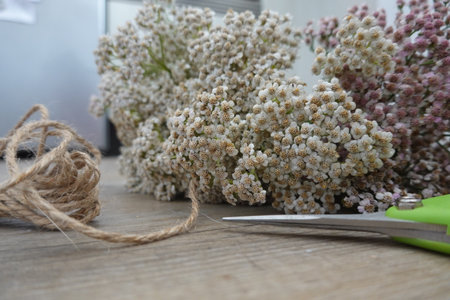 Yarrow flowers preparing for a bouquet, with rustic twine and scissors on a wooden table, focusing on floristry and craftingの写真素材