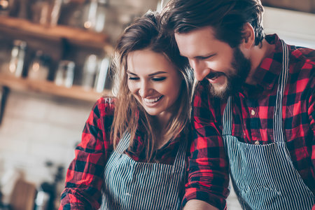 Smiling couple wearing aprons, joyfully preparing food together in the kitchen, sharing laughter and creating a delicious mealの素材