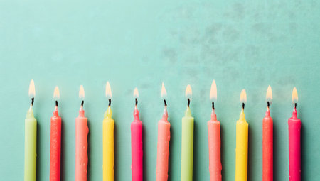 Colorful lit birthday candles burning on a teal background create a festive atmosphere, perfect for birthday celebrationsの素材