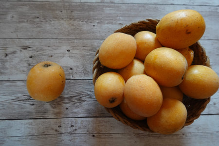 Ripe loquats, also known as Japanese plums or loquats, are presented in a wicker basket on a...