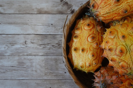 Horned melons, also known as kiwano fruit, resting in a woven basket on a light distressed wooden...