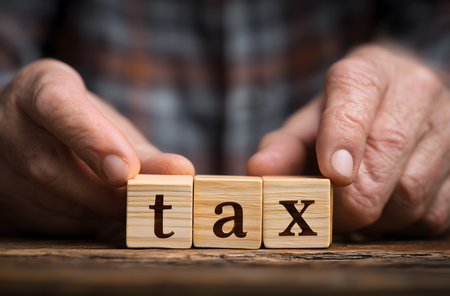 Senior person's hands forming the word tax with wooden blocks on a rustic table, representing concepts of finance and accountingの素材