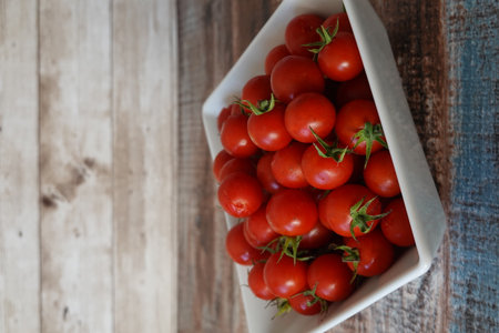 Cherry tomatoes filling a white bowl, resting on a rustic wood surface, emphasizing fresh ingredientsの写真素材