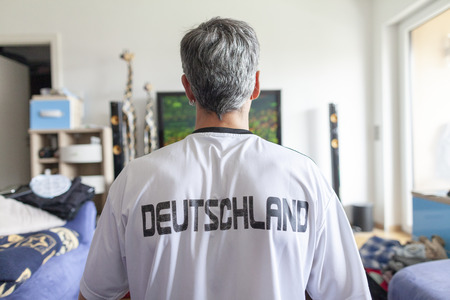 German fan sits in a Deutschland ( Germany ) jersey in front of a televisionの写真素材