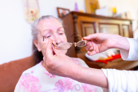 An old woman gets glasses on by a nurseの写真素材