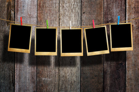 Old picture frame hanging on clothesline on wood background.
