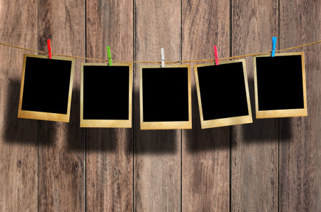 Old picture frame hanging on clothesline on wood background.
