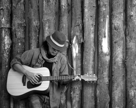 Musician playing guitar leaning timber wall. Black and white photo.の写真素材