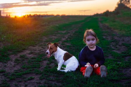 little girl and dog are resting sitting on the ground in the parkの写真素材