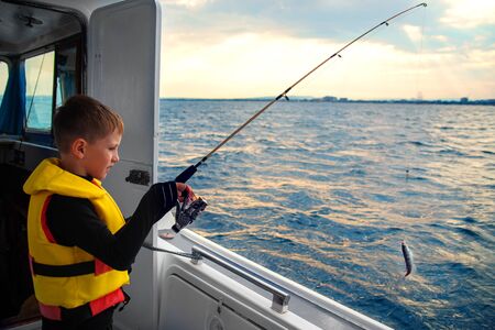 little boy caught fish spinning from a boat at seaの写真素材