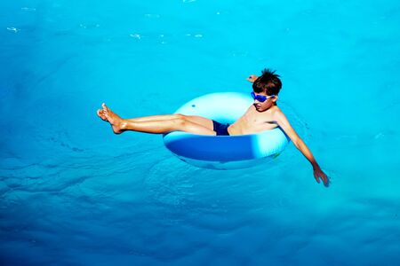 Beautiful young boy with inflatable ring relaxing in blue swimming poolの写真素材
