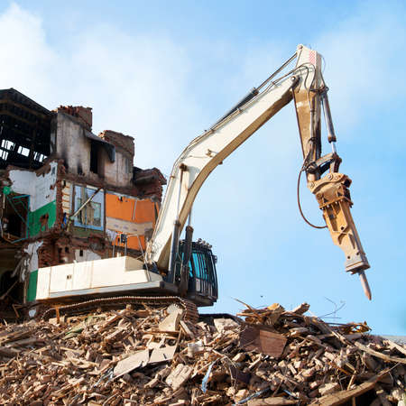 excavator demolishing a brick building. Machinery Demolishing Buildingの写真素材