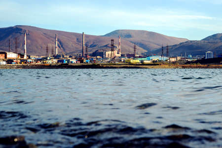 The shore of a polluted lake against the backdrop of a metallurgical plant in the city of Norilsk.の写真素材