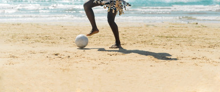 Black man playing soccer on the beach. Beach football. Panoramic photo.