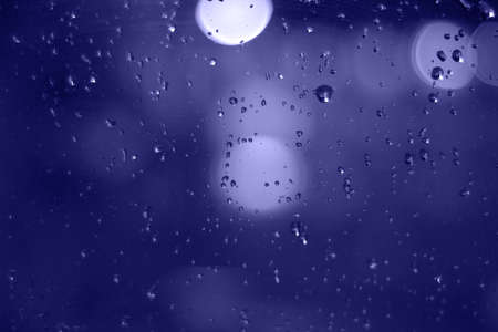 Rain drops with bokeh effect in the night city. Drops of rain on window with abstract lights.の写真素材
