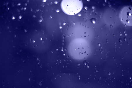 Rain drops with bokeh effect in the night city. Drops of rain on window with abstract lightsの写真素材