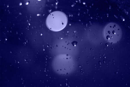Rain drops with bokeh effect in the night city. Drops of rain on window with abstract lightsの写真素材