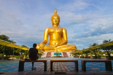 a single man is sitting in front of big golden buddhaの写真素材