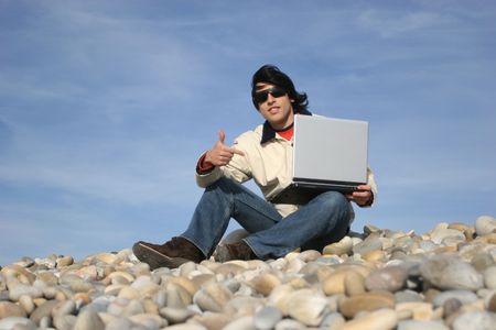 young casual man with laptop at the beach, isolated on blue sky backgroundの写真素材