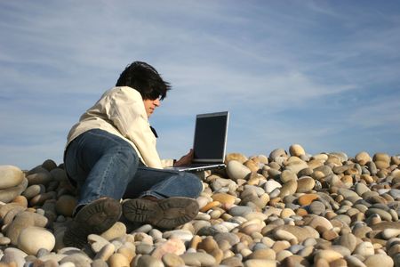 young casual man with laptop at the beach, isolated on blue sky backgroundの写真素材