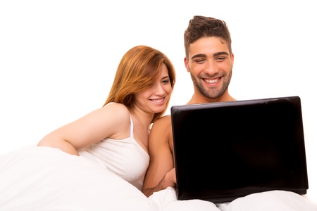 Happy couple watching a movie in bedの写真素材