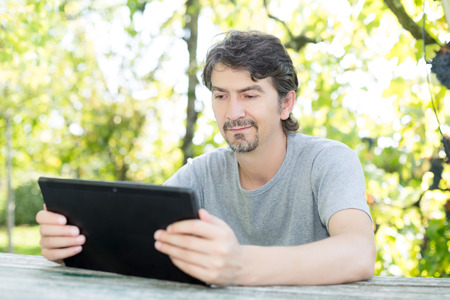 Young man relaxing with a tablet computer at a gardenの写真素材
