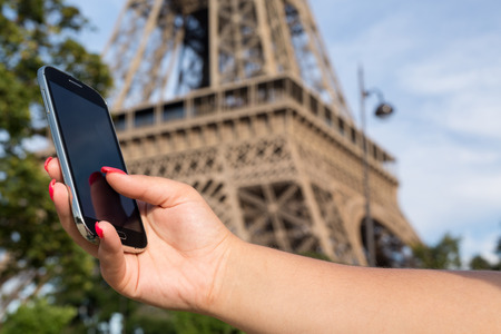 Woman consulting her smartphone with Eiffel Tower on backgroundの写真素材