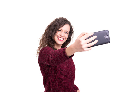 Happy young woman taking self portrait photography through smart phone over white background.の写真素材