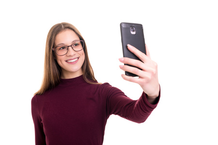 Happy young woman taking self portrait photography through smart phone over white background.の写真素材