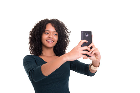 Happy young woman taking self portrait photography through smart phone over white background.の写真素材