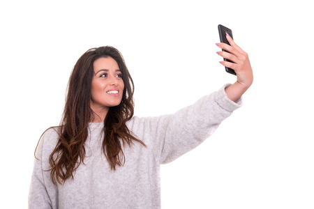 Happy young woman taking self portrait photography through smart phone over white background.の写真素材