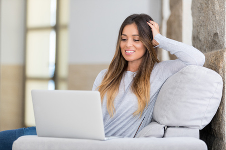 Beautiful young woman relaxing at home on her laptop computerの写真素材