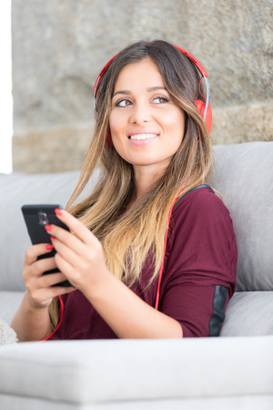 Beautiful young woman relaxing on couch while listening to some musicの写真素材