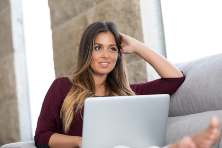 Beautiful young woman relaxing at home on her laptop computerの写真素材