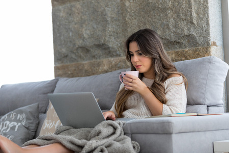 Beautiful young woman relaxing at home on her laptop computerの写真素材